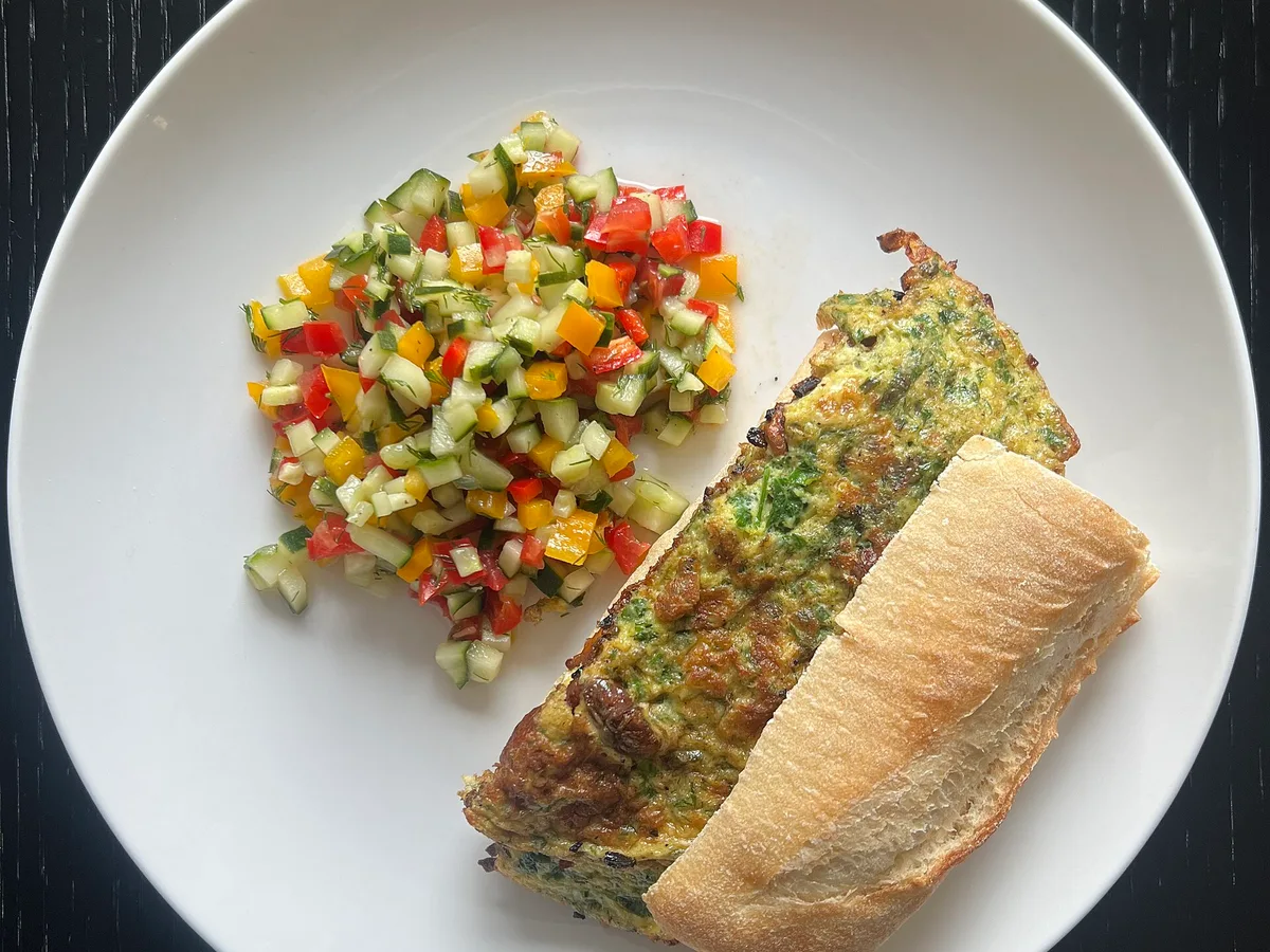 Kräuteromelett mit klein geschnittenem Salat und einem Stück Baguette auf einem weißen Teller