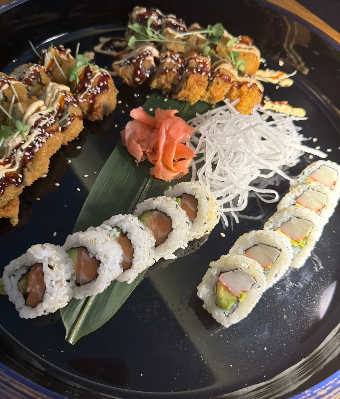 Schwarzer Teller mit verschiedenen Sushi-Rollen, eingelegtem Ingwer und Rettichstreifen