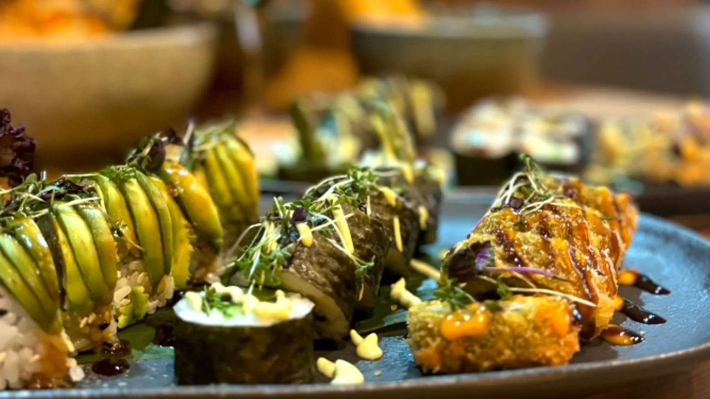 Sushi-Rollen mit Avocadofächer und Nori auf blauem Teller, garniert mit Kresse und Sauce