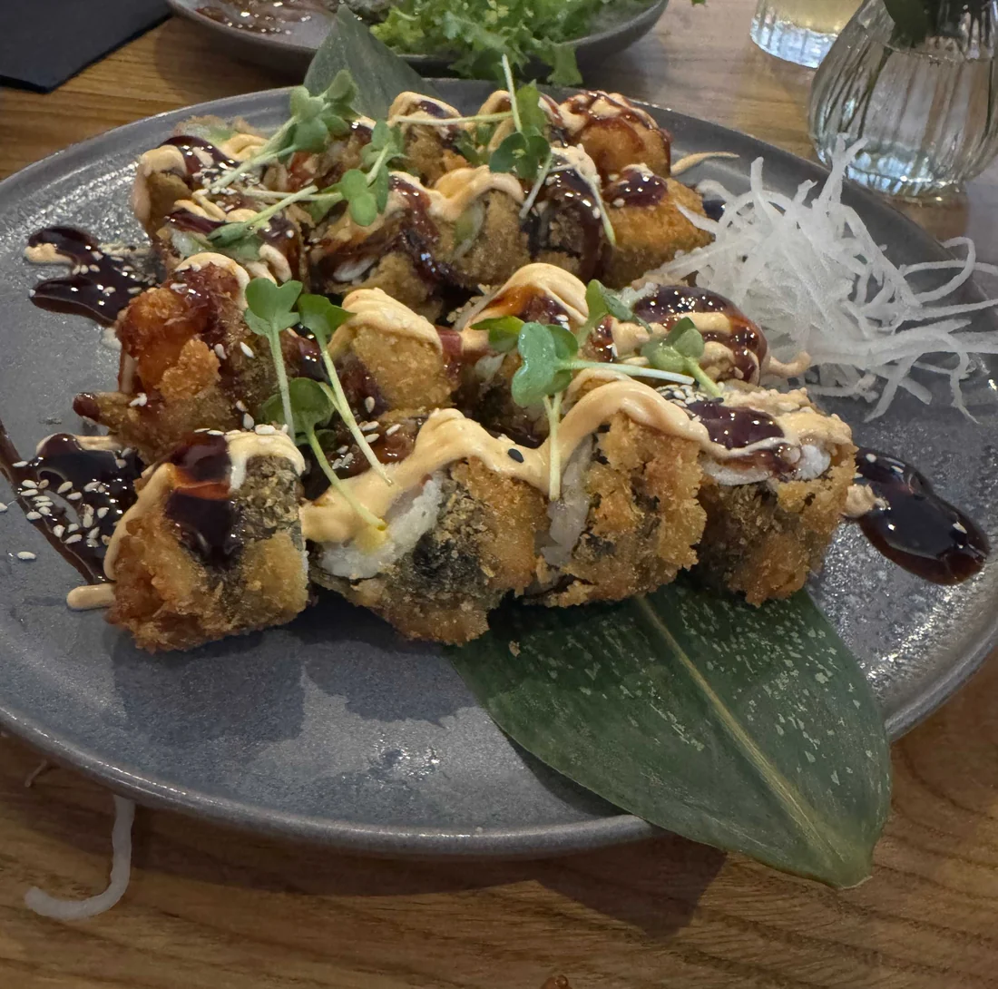 Frittierte Sushi-Rollen mit dunkler Sauce und Mayonnaise auf grauem Teller