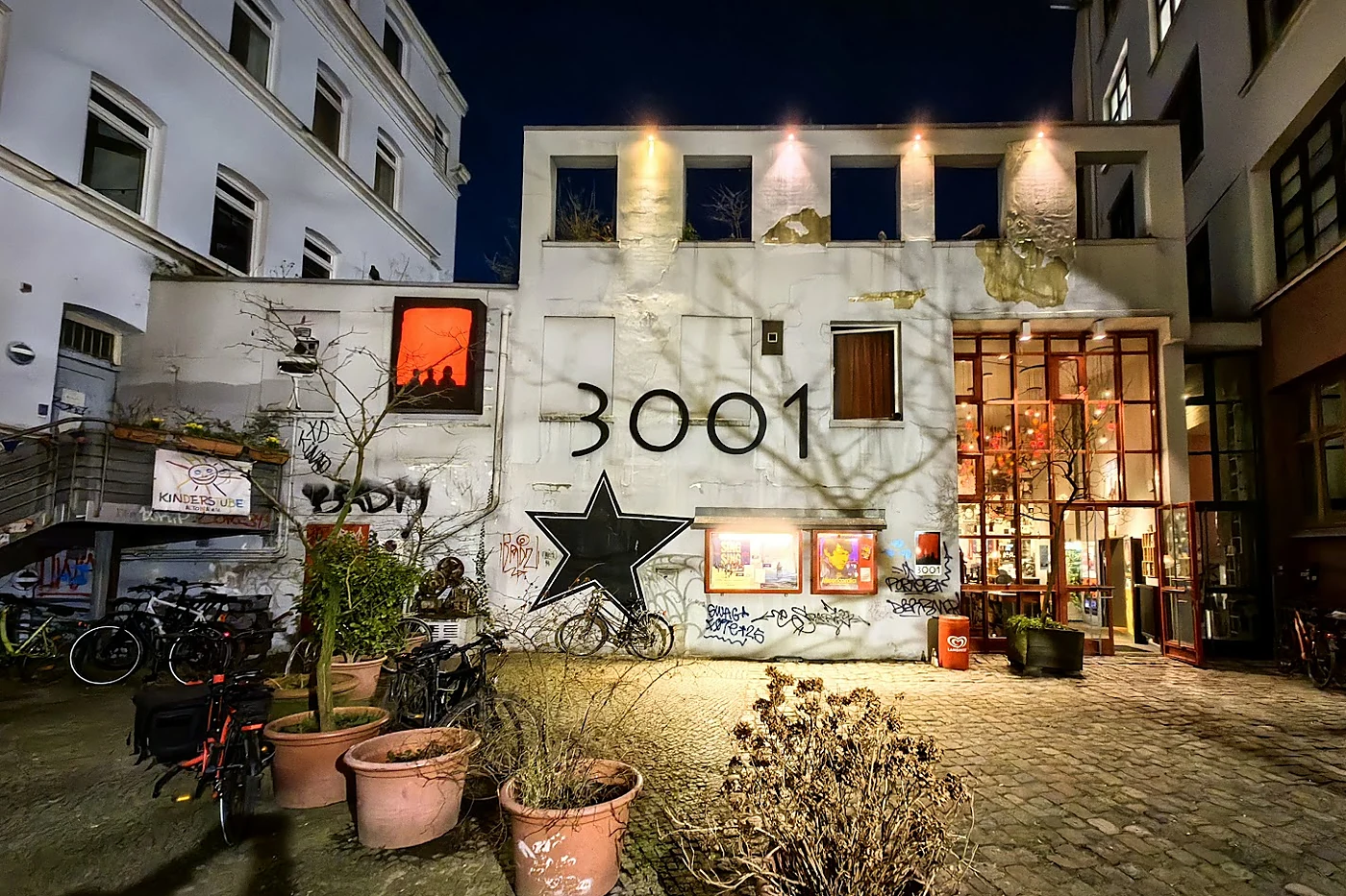 Beleuchteter Hinterhof bei Nacht mit der Zahl 3001 und einem großen schwarzen Stern an einer weißen Wand