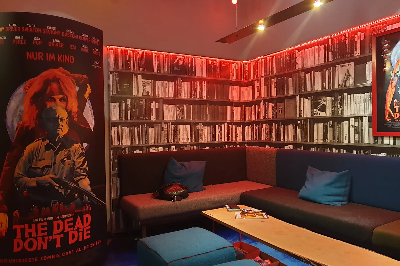 Kinolounge mit Ecksofa, Kissen, niedrigem Holztisch, Tapete mit Bücherregalmotiv und rotem Lichtband