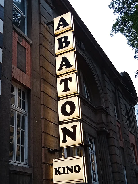 Senkrechtes beleuchtetes Leuchtschild mit den Buchstaben ABATON und einem Kasten mit der Aufschrift KINO an einer Steinf