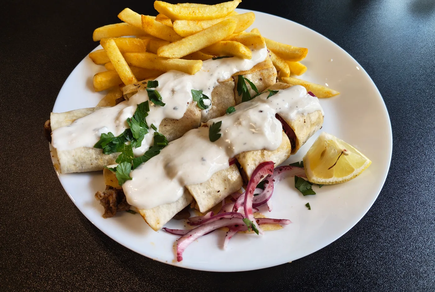 Zwei Tantuni-Rollen mit Joghurtsauce, Petersilie und Zwiebeln, dazu Pommes und Zitrone