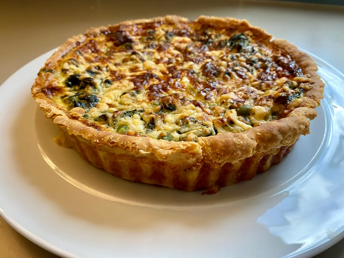 Runde Quiche mit Käse und Gemüse in einem Mürbeteigboden auf einem weißen Teller