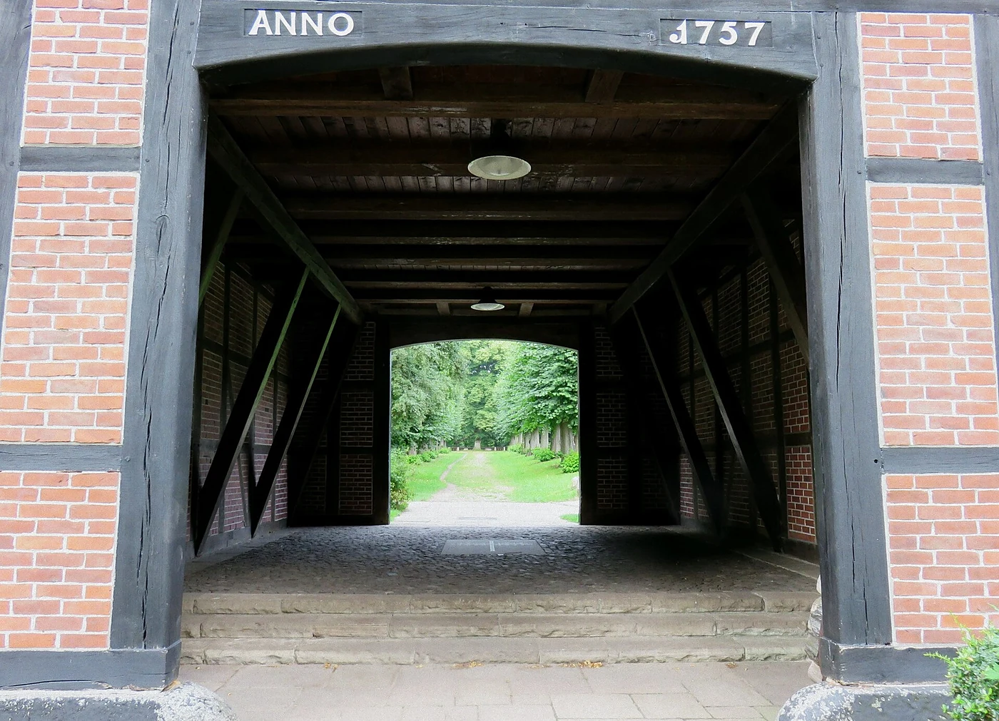 Blick durch die gewölbte Durchfahrt des Torhauses mit der Inschrift „Anno 1757“ auf die Allee zum Herrenhaus
