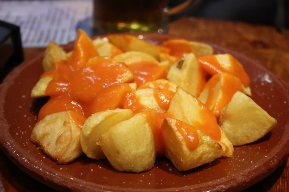 Patatas bravas mit roter Sauce auf einem Tonteller