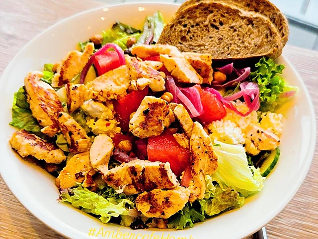 Salat mit gegrilltem Hähnchen, Tomaten, roten Zwiebeln und einer Scheibe Brot in einer weißen Schale