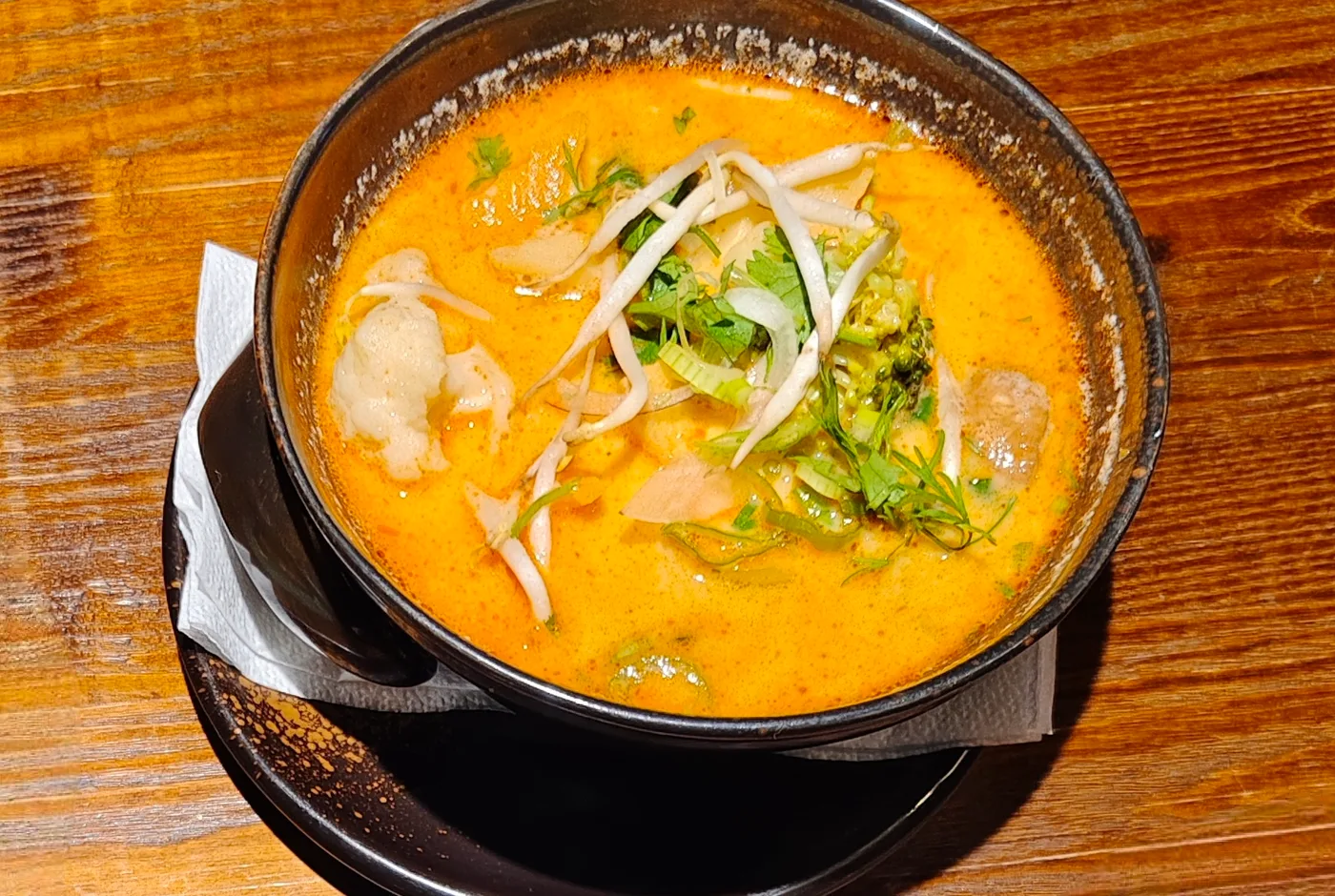 Kokossuppe in einer dunklen Keramikschale mit Sprossen, Koriander und Brokkoli