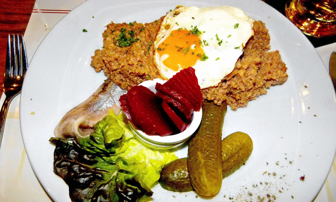 Labskaus mit Spiegelei, Matjes, Roter Bete und Gewürzgurke auf weißem Teller