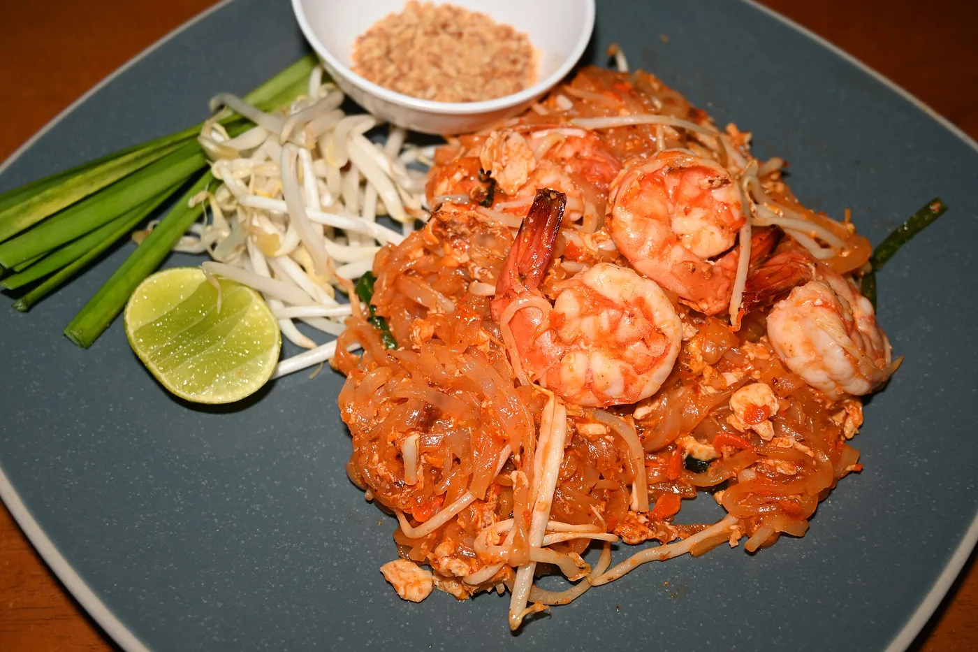 Pad Thai mit Garnelen, Limette, Sprossen und Erdnüssen auf blauem Teller