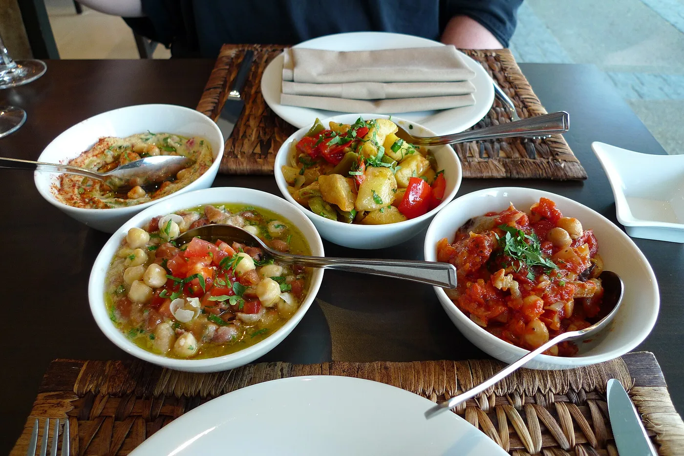Vier Schalen mit Hummus, Kichererbsen, Gemüse und Auberginen auf einem Tisch