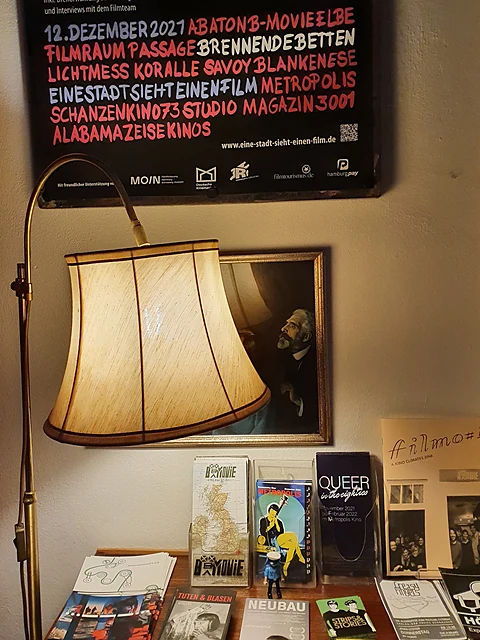 Foyerecke mit Messing-Stehlampe, gerahmtem Gemälde und einem Tisch voller Programmhefte und Flyer