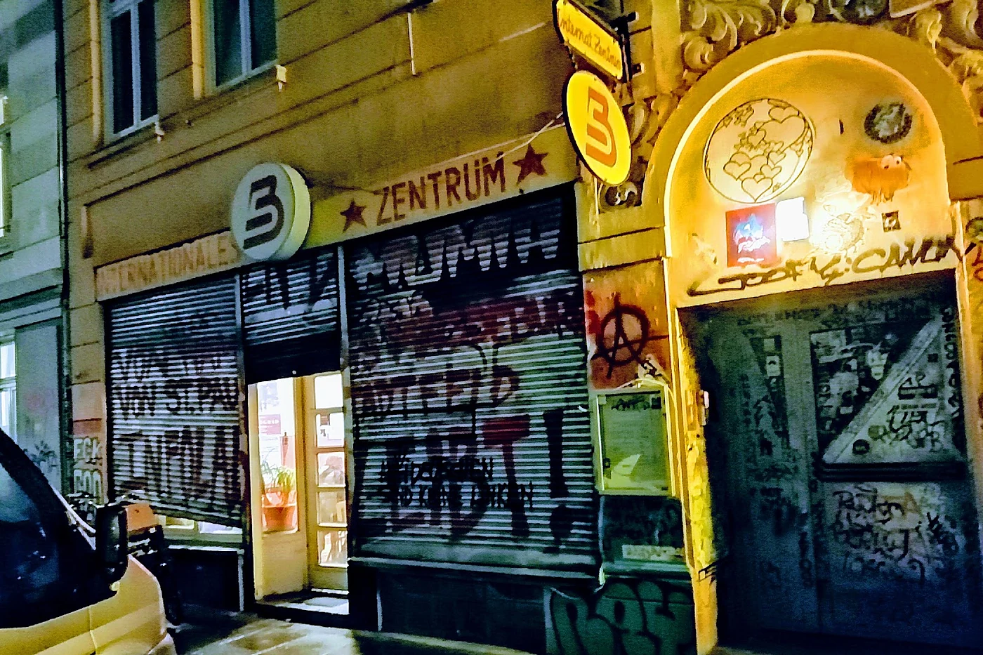 Beleuchtete Altbaufassade bei Nacht mit rundem B-Logo, der Aufschrift Internationales Zentrum und Graffiti auf den Rolll