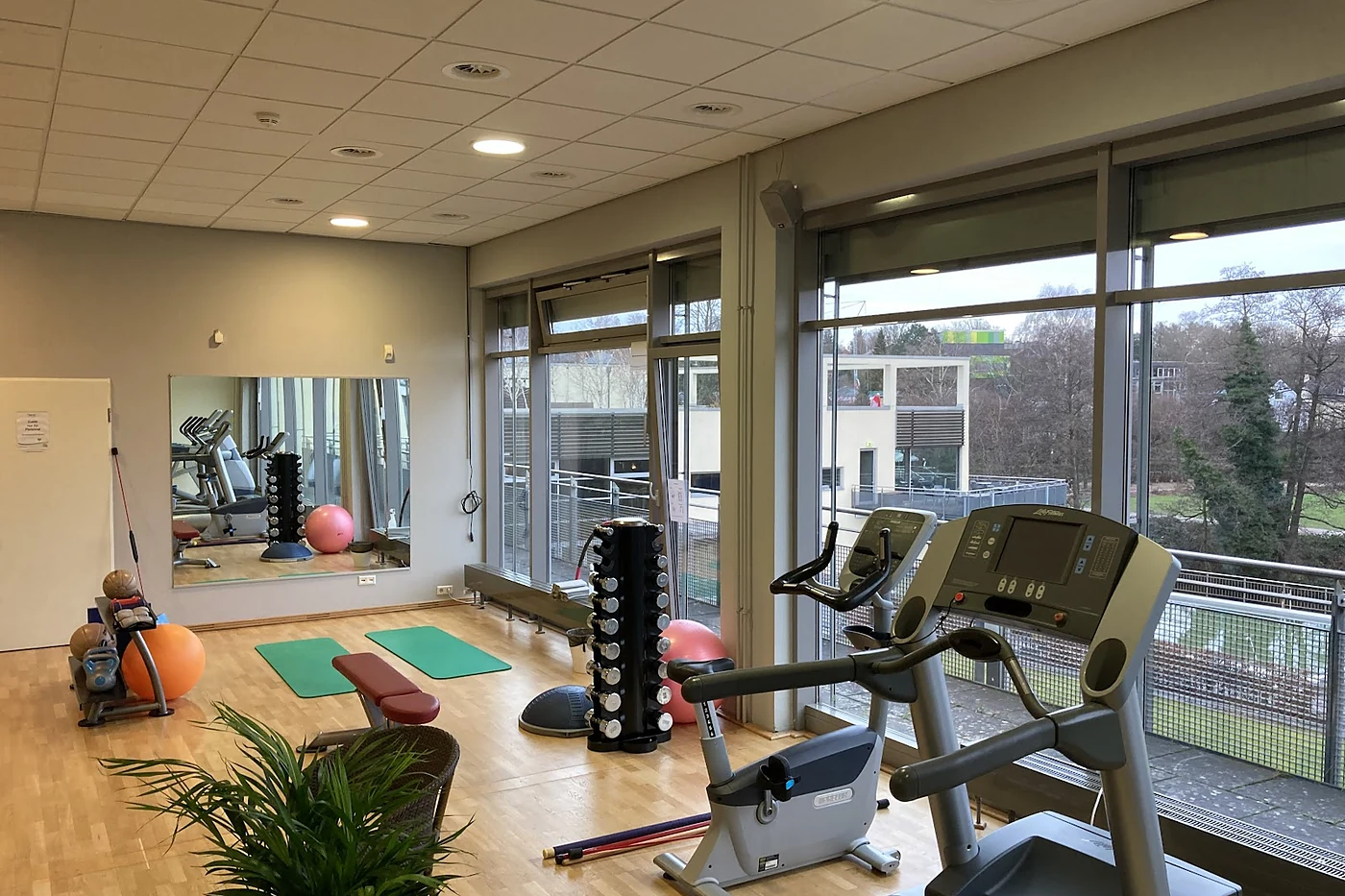 Fitnessbereich mit Geräten vor bodentiefen Fenstern