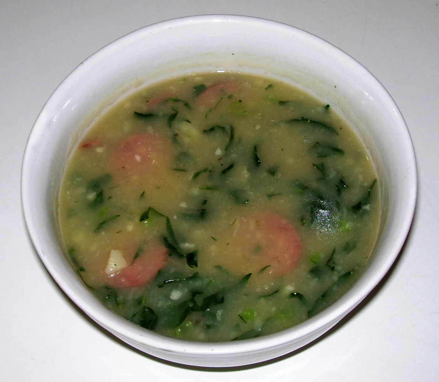 Caldo Verde, portugiesische Grünkohlsuppe mit Wurstscheiben in weißer Schale