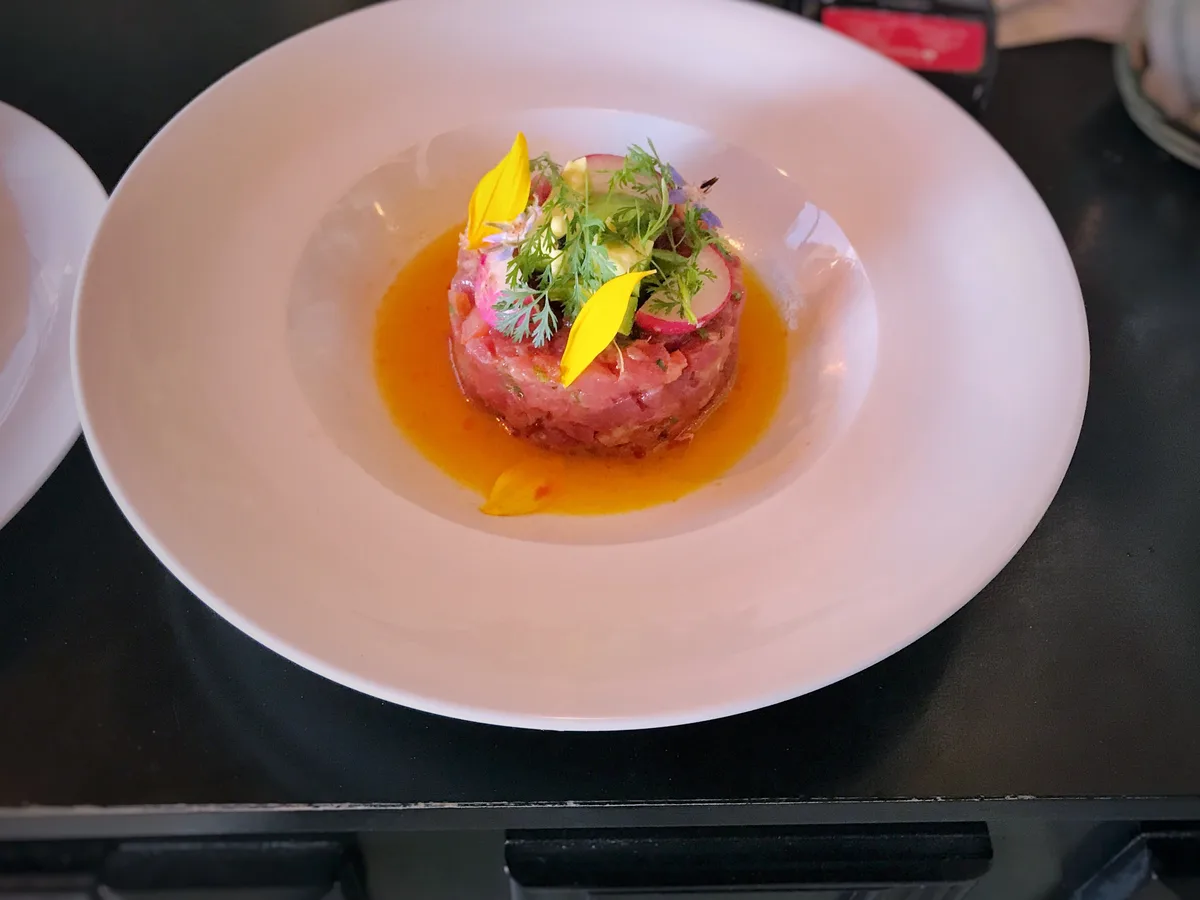 Thunfisch-Tatar als Törtchen mit Kräutern und essbaren Blüten in einem tiefen weißen Teller