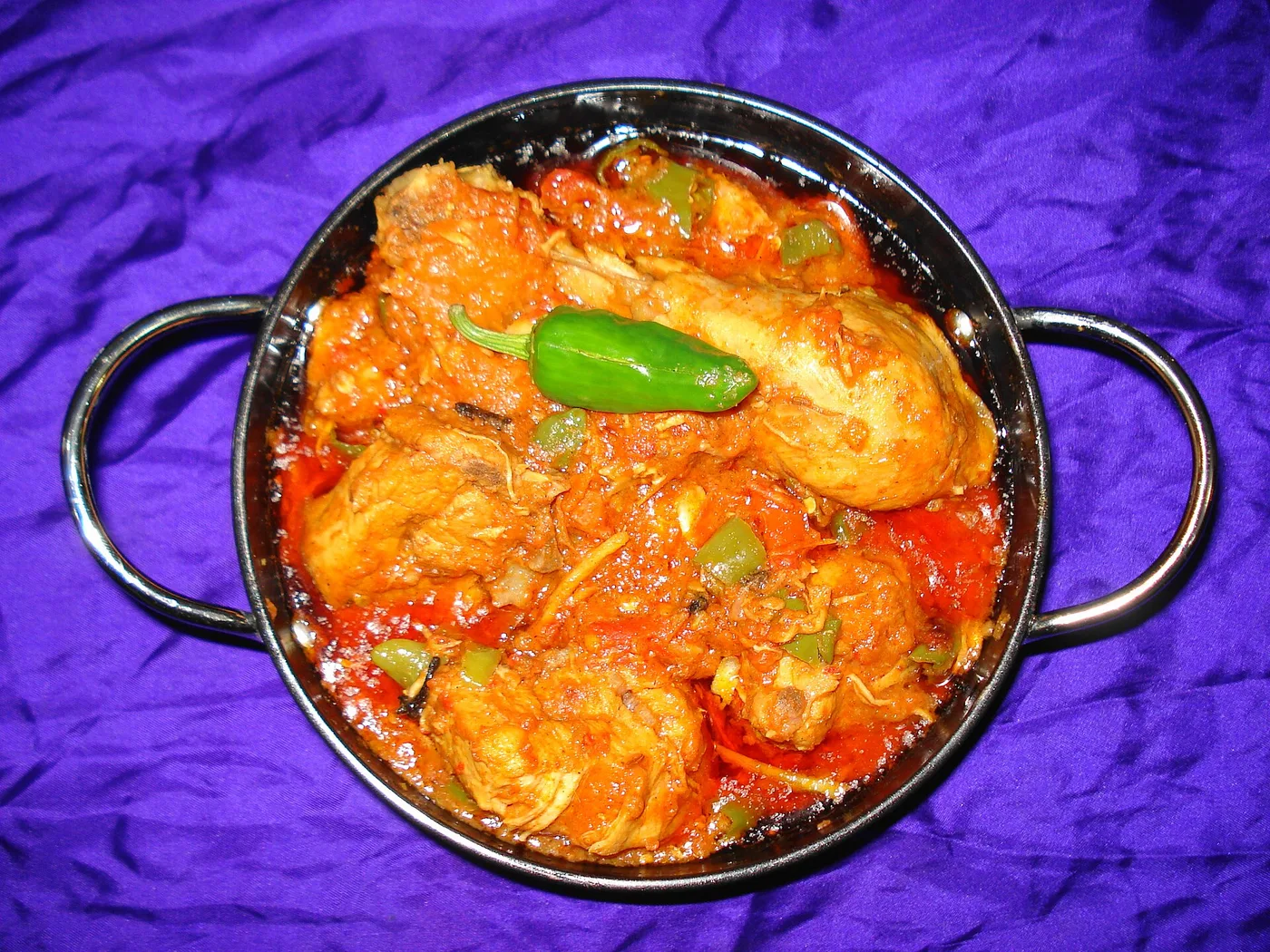 Chicken Karahi in einer Eisenpfanne mit Tomaten, Paprika und grüner Chili
