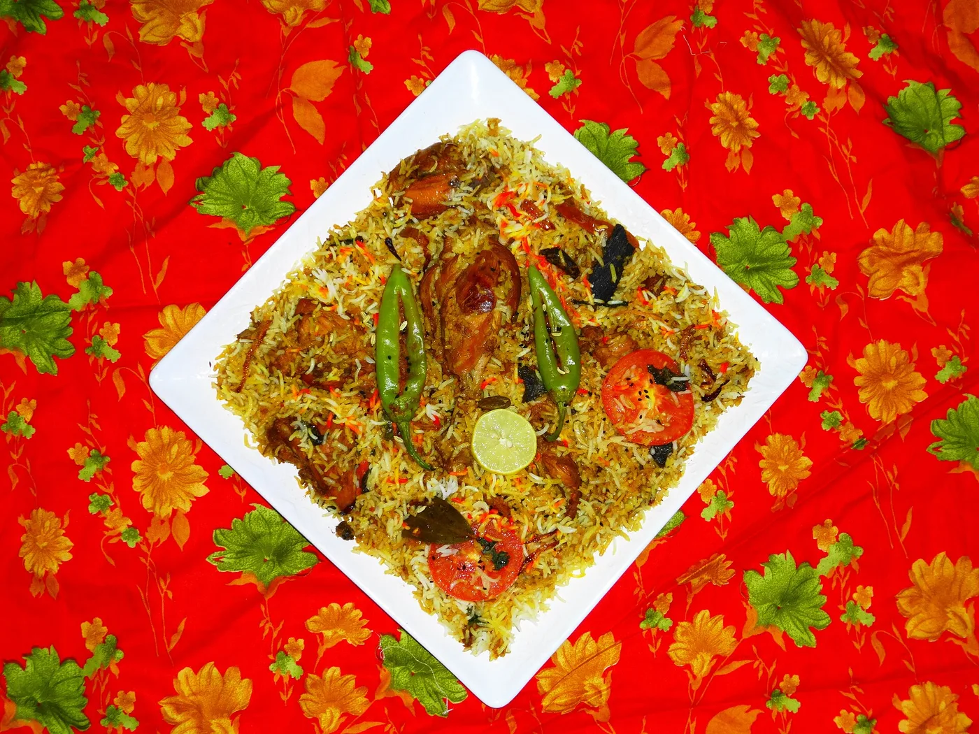 Biryani mit Hähnchen, grünen Chilis und Tomaten auf weißem Teller