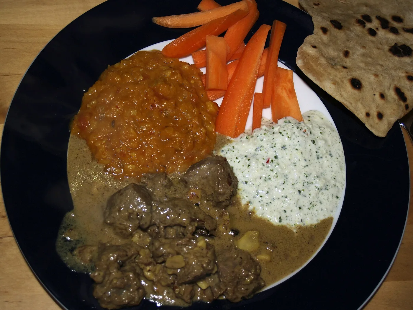Lammkorma mit Linsen, Raita, Karotten und Fladenbrot auf einem Teller