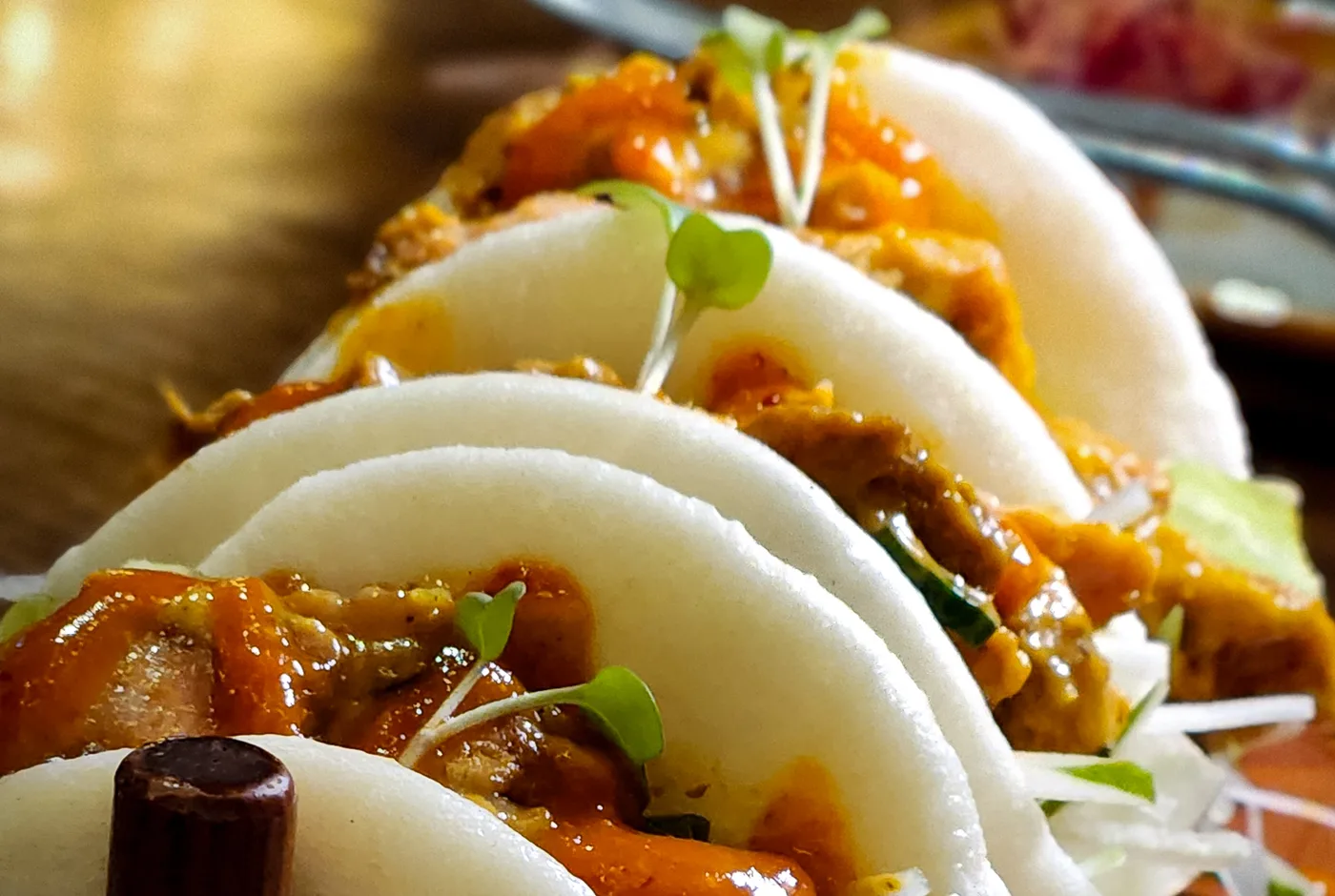 Vier gedämpfte Bao-Brötchen mit geschmortem Fleisch, Sauce und Kresse auf einem Holzbrett