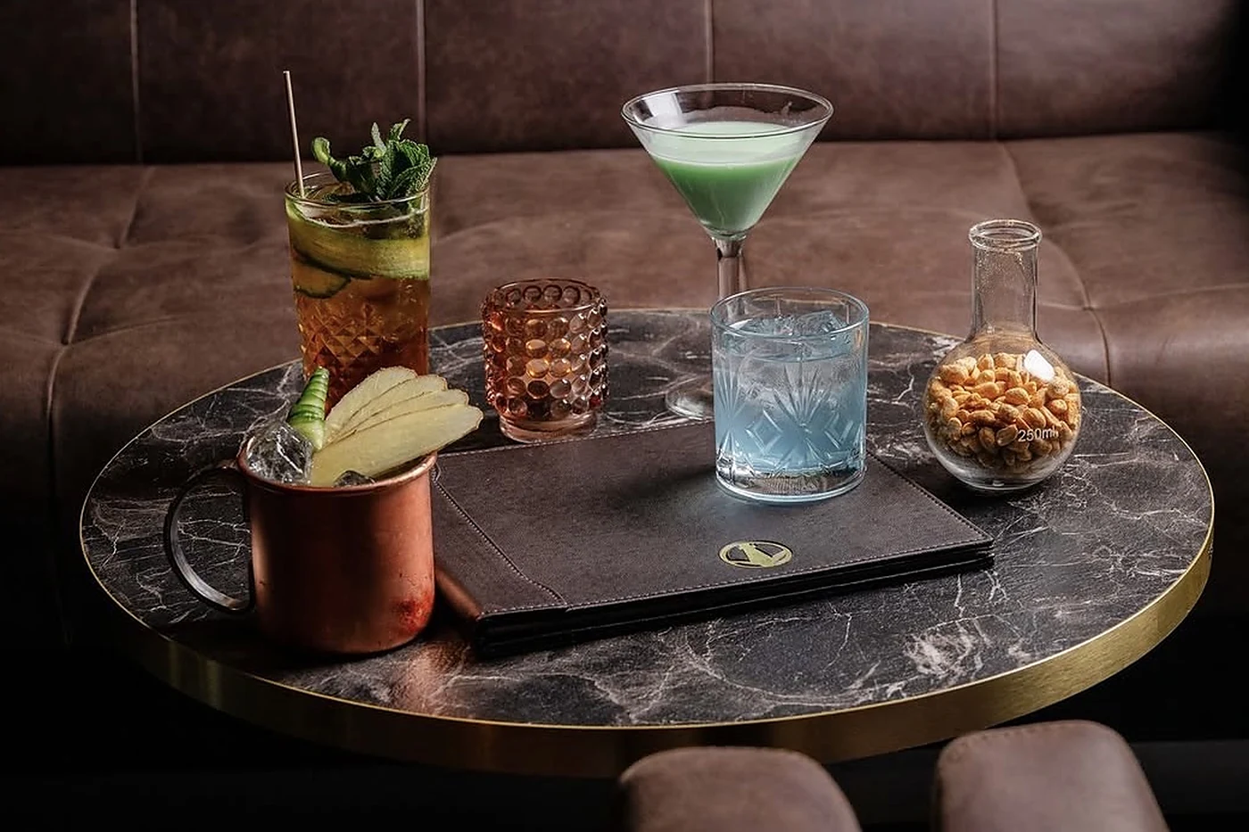 Marmortisch mit vier Drinks: Kupferbecher, Longdrink mit Minze, grüner Cocktail im Martiniglas, blauer Drink und ein Gla