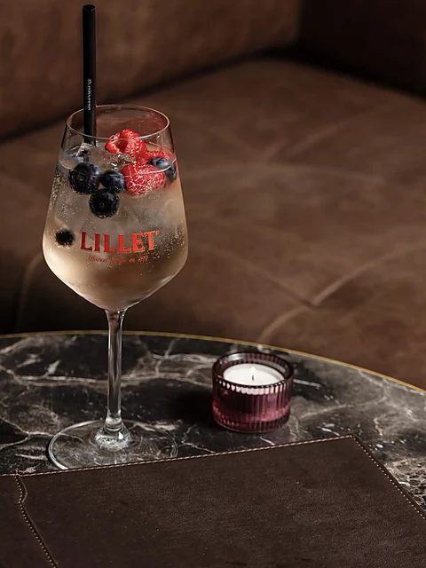 Lillet Spritz mit Beeren im Weinglas neben einer Kerze auf einem Marmortisch
