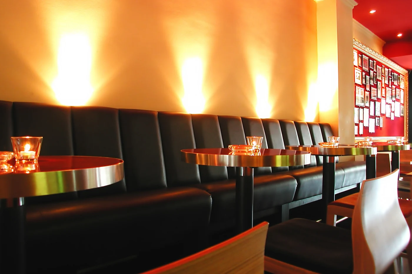 Lederbank mit runden Tischen in der Bar, rechts eine rote Wand voller gerahmter Autogrammkarten