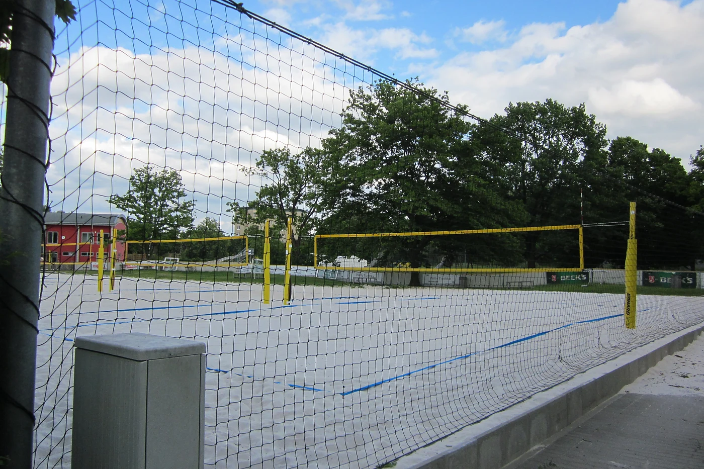 Außenfelder mit Beachvolleyballnetzen, dahinter die rote Halle