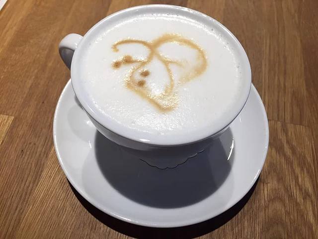 Cappuccino mit Milchschaum und Kakaomuster in weißer Tasse auf einem Holztisch