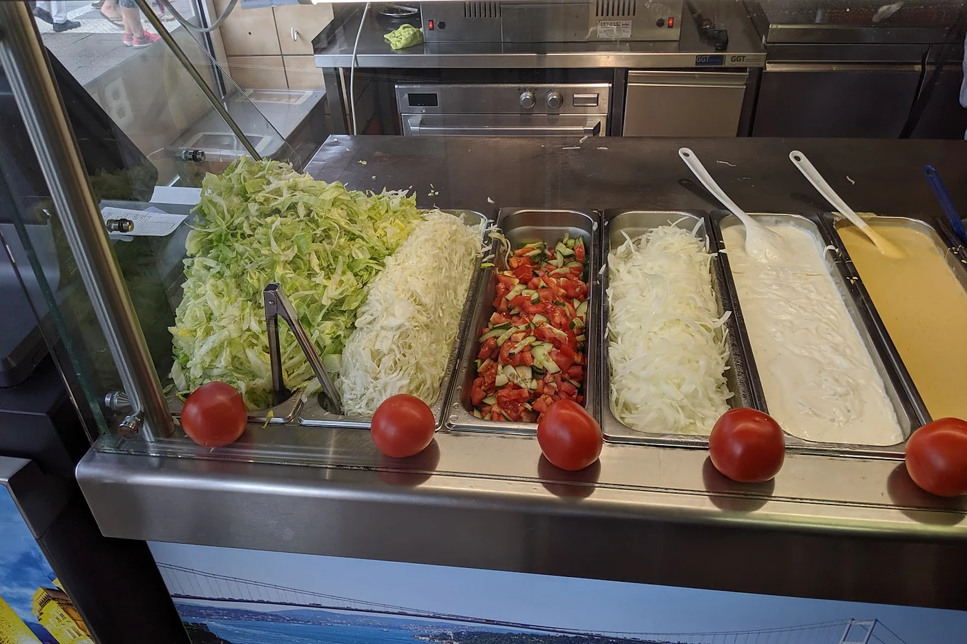 Salattheke mit Krautsalat, Tomaten und Soßen hinter Glas