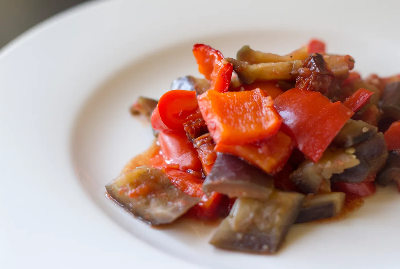 Caponata aus Auberginen, Paprika und Tomaten auf einem weißen Teller