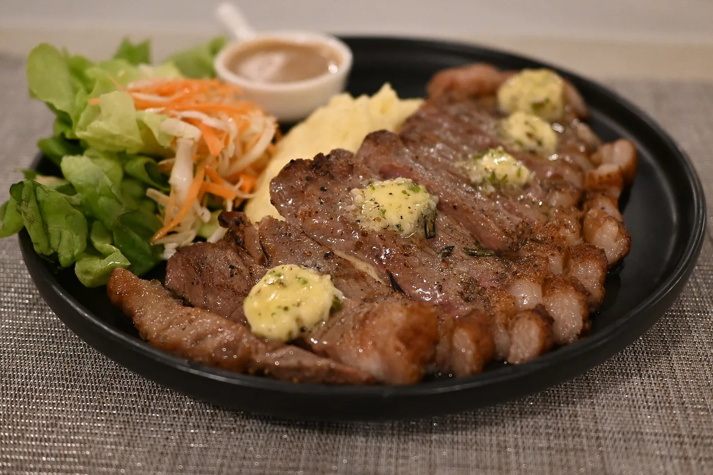 Gebratenes Steak mit Kräuterbutter, Kartoffelpüree und Salat auf schwarzem Teller