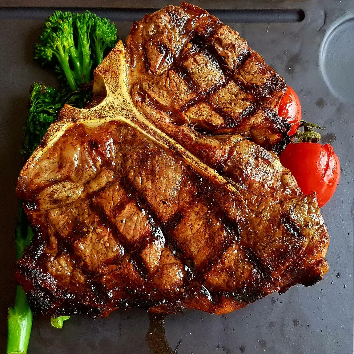 Gegrilltes T-Bone-Steak mit Grillmuster, Brokkoli und Kirschtomaten auf grauer Platte