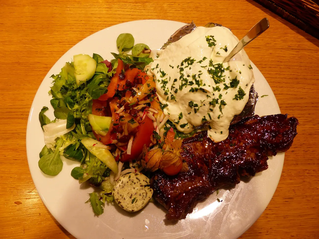 Steak mit Ofenkartoffel, Sauerrahm, Salat und Kräuterbutter auf einem weißen Teller