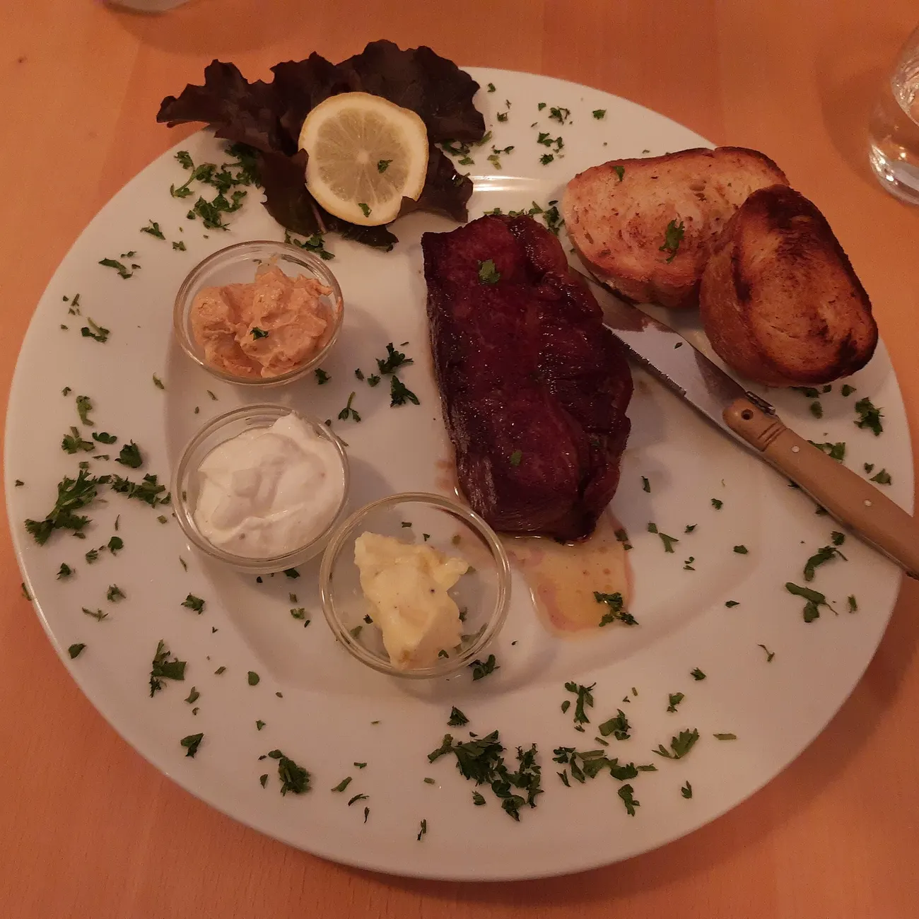 Steak mit geröstetem Weißbrot und drei Schälchen mit Butter, Sauerrahm und Kräuterbutter