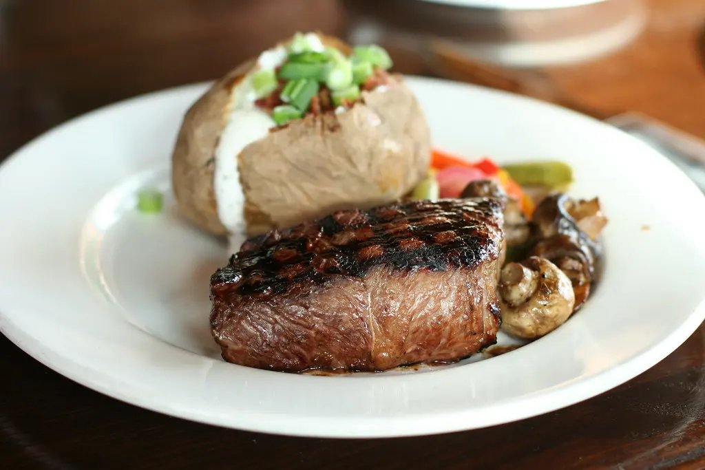 Gebratenes Steak mit Kräuterbutter, Kartoffelpüree und Salat auf schwarzem Teller