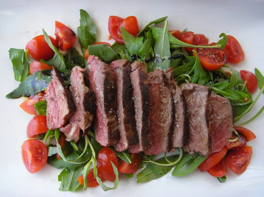 Gebratenes Steak mit Kräuterbutter, Kartoffelpüree und Salat auf schwarzem Teller