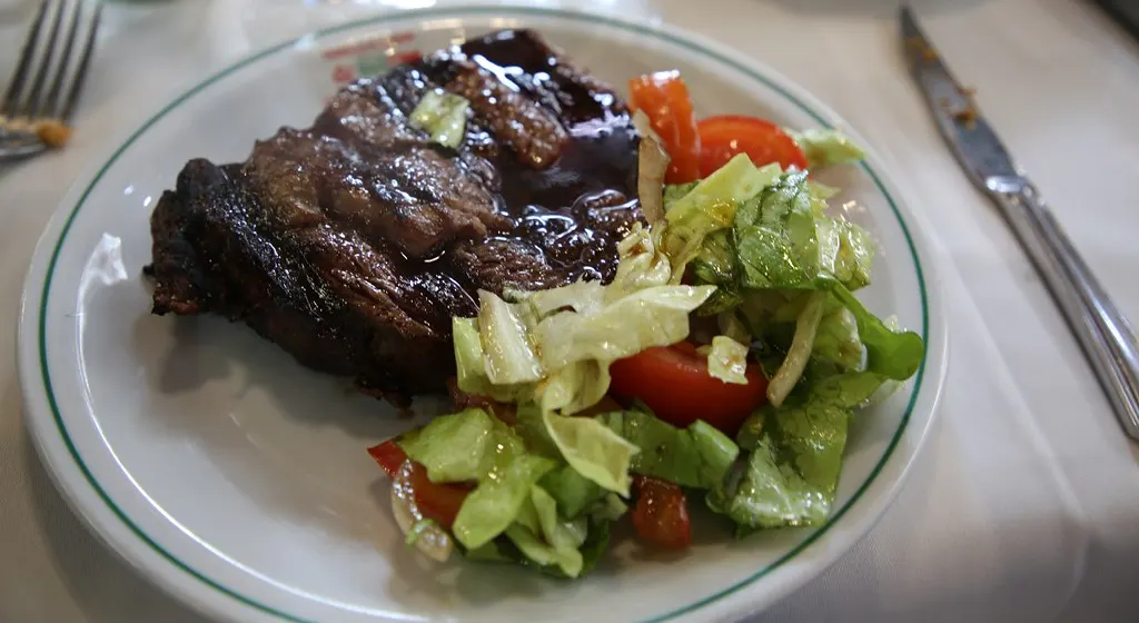Steak mit grünem Salat und Tomaten auf einem weißen Teller mit grünem Rand