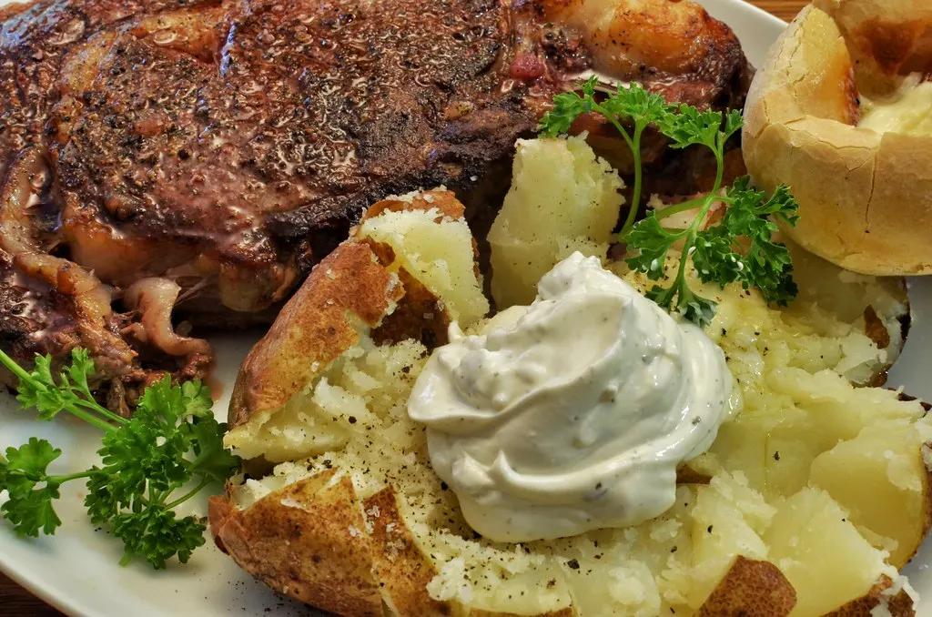 Ribeye-Steak neben einer aufgeschnittenen Ofenkartoffel mit Sauerrahm und Petersilie