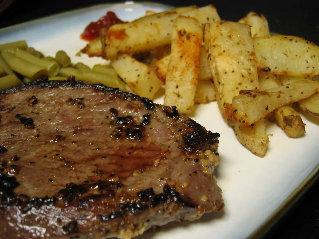 Gebratenes Steak mit Kartoffelspalten und grünen Bohnen auf weißem Teller