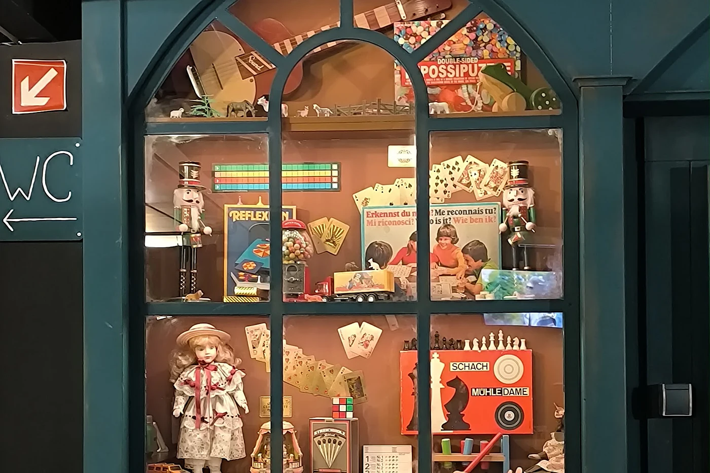 Beleuchtete Schaufenstervitrine mit alten Gesellschaftsspielen, Spielkarten, Nussknackern und einer Porzellanpuppe