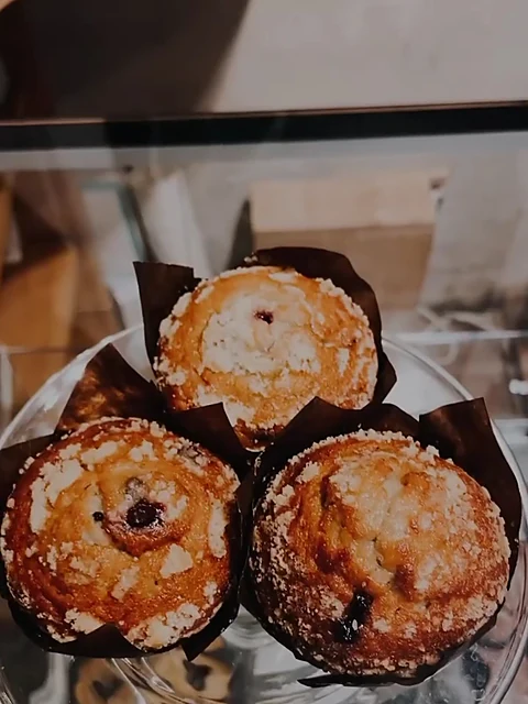 Drei Muffins mit Streuseln in braunen Papierförmchen auf einer Glasplatte in der Vitrine