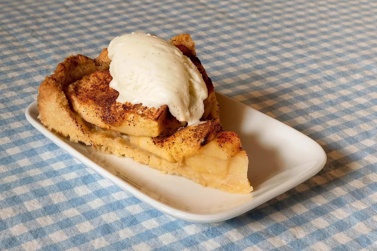 Stück Apfelkuchen mit einer Kugel Vanilleeis auf einem länglichen weißen Teller
