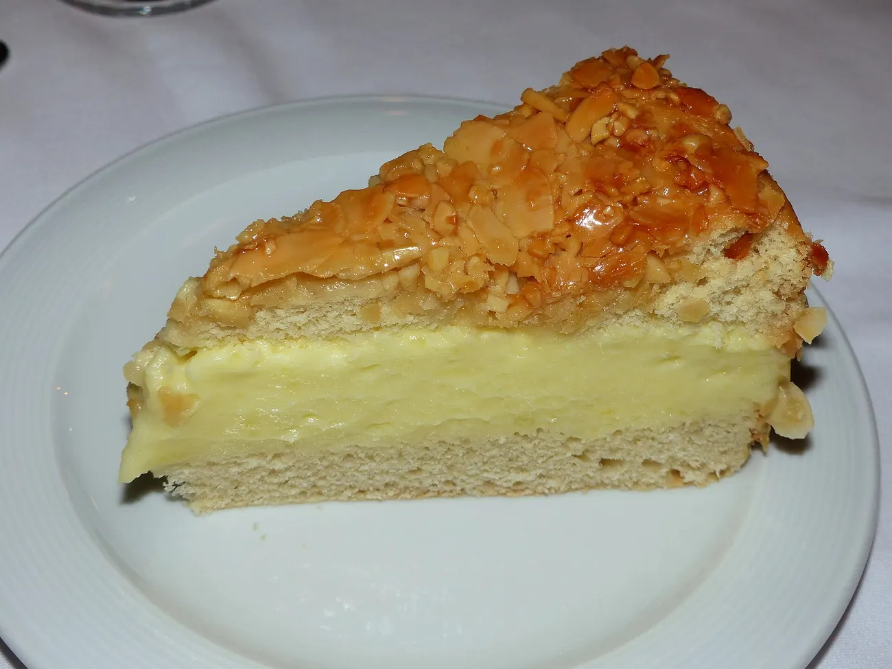 Stück Bienenstich mit Mandelkruste und heller Puddingcreme auf weißem Teller
