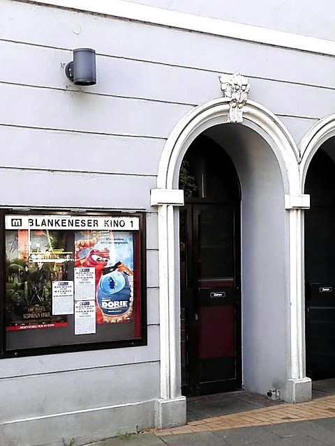 Weiß verputzte Fassade mit Rundbogen-Eingang und Schaukasten mit der Aufschrift Blankeneser Kino 1