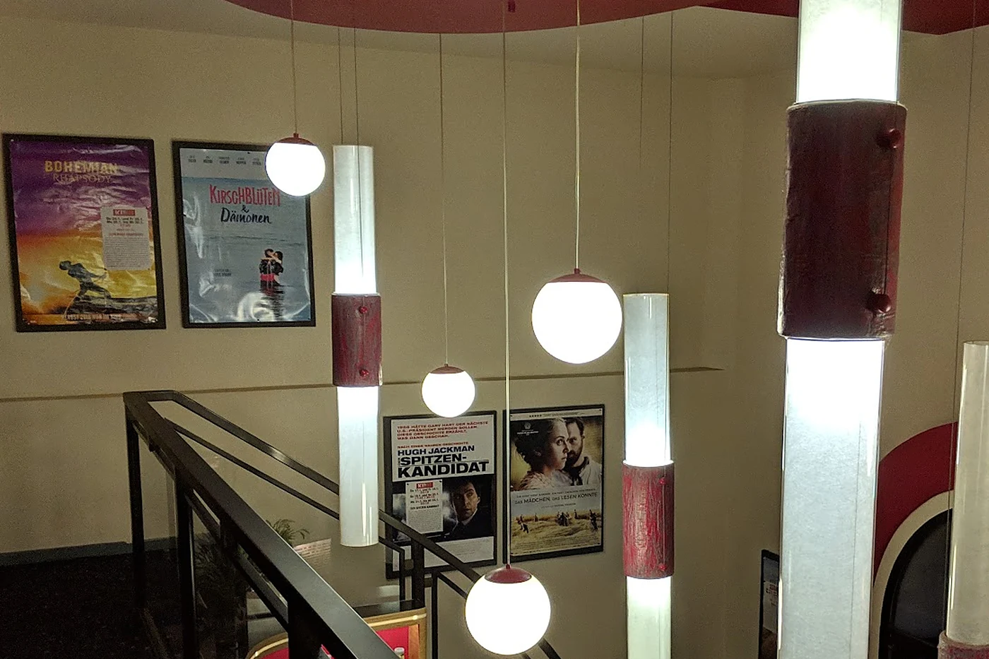 Foyer mit gerahmten Filmplakaten, Treppengeländer und eigens gestalteten Hänge- und Stableuchten