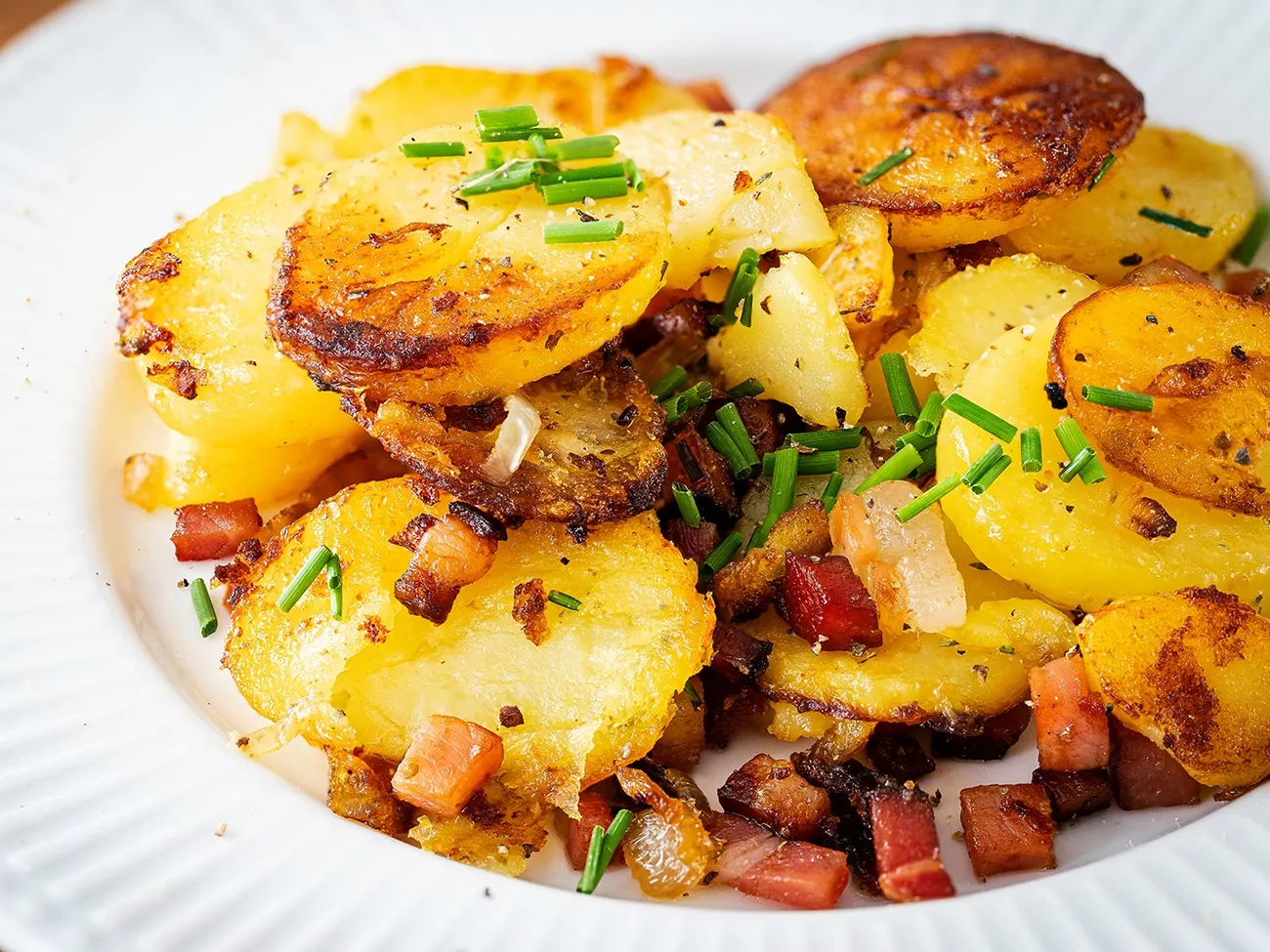 Bratkartoffeln mit Speckwürfeln und Schnittlauch auf einem weißen Teller