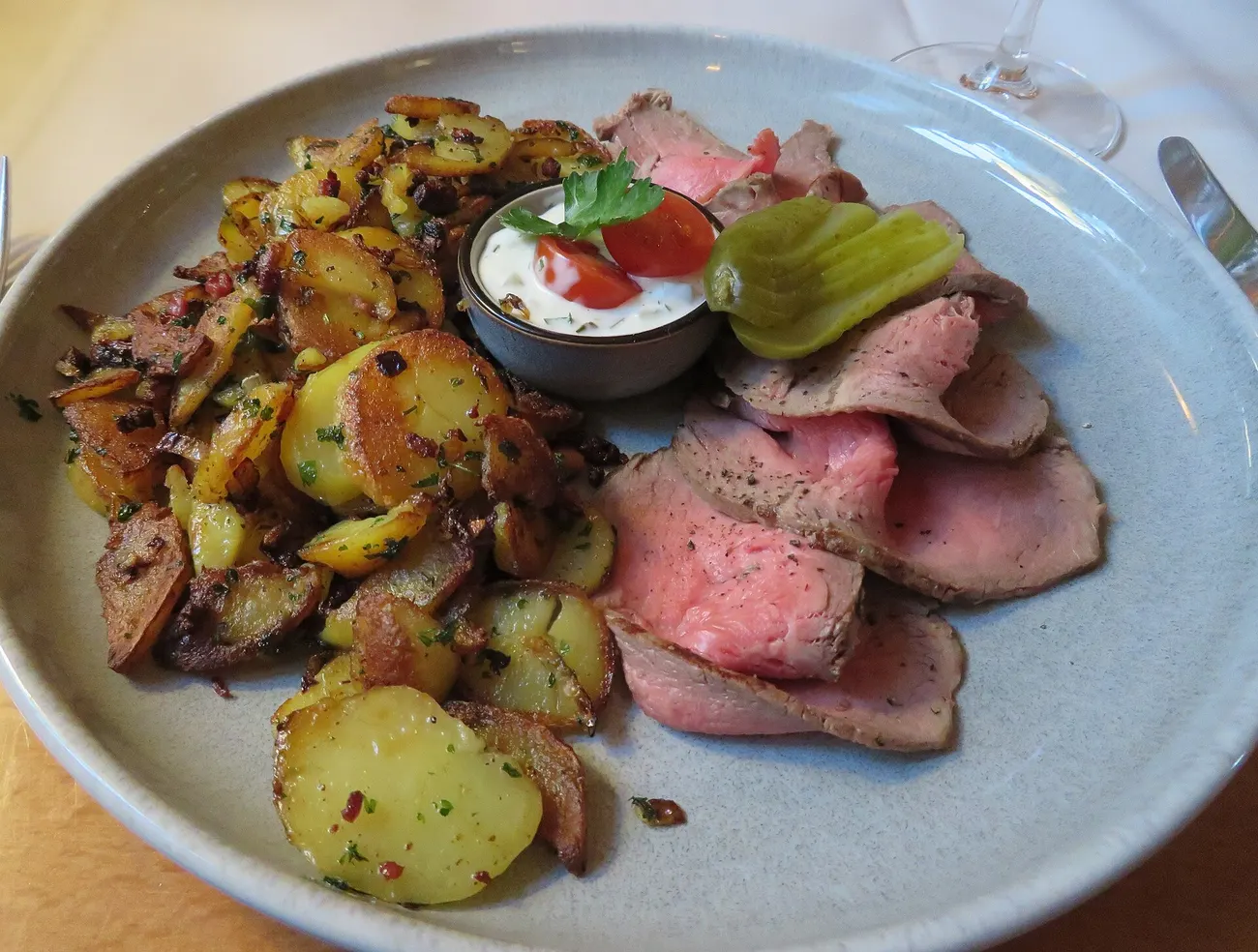 Roastbeef in Scheiben mit Bratkartoffeln, Remoulade und Gewürzgurke auf grauem Teller