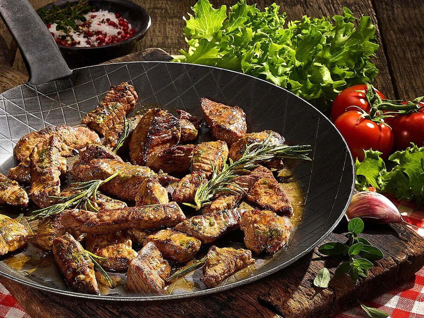 Pfanne mit gebratenen Steakstreifen, Rosmarin, Tomaten und Salat